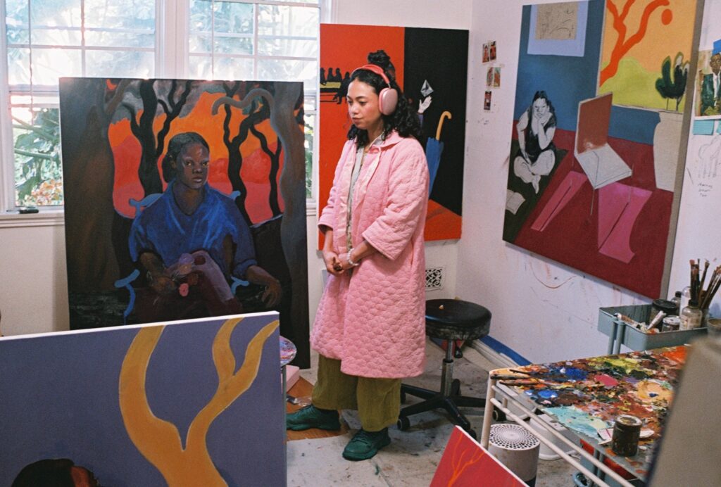 Portrait of artist Hana Ward in her studio surrounded by paintings