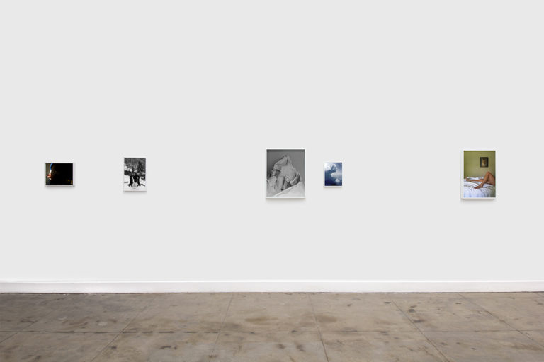 Installation image of Ohan Breiding's Playing Submarine show, of about five portraits hanging on the wall. The first one is a man is holding like a cottage cheese object with a right hand that closes to his abdomen. The second one is a black and white picture of a furry dog that is doing chin-up. The third one is a white crumbled paper shaped-like a mountain. The fourth one is a photo of cumulonimbus clouds and the last one shows a light-medium-skinned woman laying on the bed and showing her legs