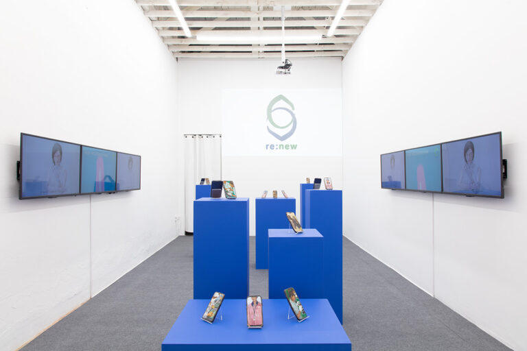Installation image of Young Joo Lee's Lizardians containing blue pedastels topped with glazed ceramic sculptures, a 3-channel video installation, and the artist's "Re:new" logo.